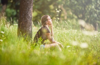 放松的女孩坐在树下在草甸在夏天天