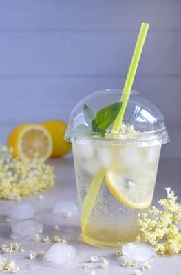自制接骨柠檬汁与柠檬和接骨木莓花在塑料杯与球形圆顶帽和鸡尾酒管.